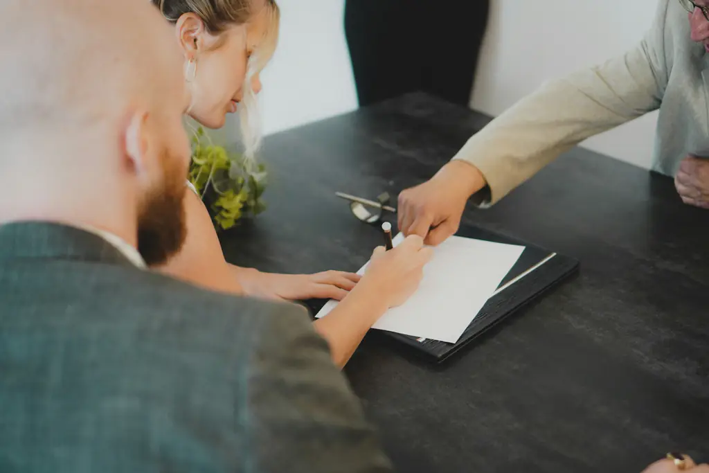 Two people signing a document across a table from a third