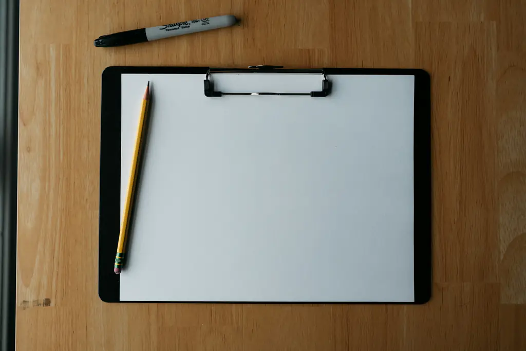 An empty clipboard, pencil and pen laid out on a timber surface