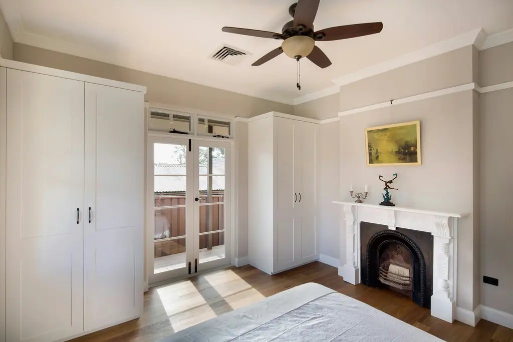 A bedroom with built-in wardrobes, an original fireplace and French doors onto a balcony